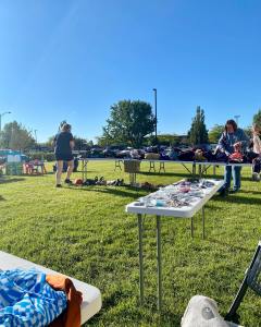 An outdoor community event showing a registration table with brochures and staff members interacting with the public on a sunny day.