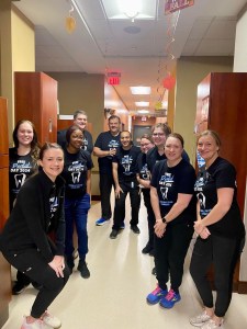 A large group of staff members in matching black clinic t-shirts smiling and posing in a long office hallway