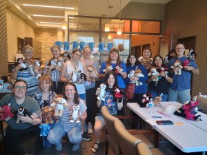 A large group of smiling staff members posing together in a modern office lobby, with many individuals holding up small stuffed animal toys